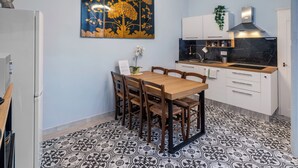 Una cocina moderna con comedor, que presenta un suelo con estampado blanco y negro, una mesa de comedor de madera con sillas, un cuadro decorativo grande y una estufa empotrada.