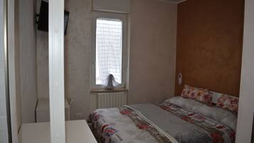 Un dormitorio con cama, ventana con cortina, radiador y televisor instalado en la pared.