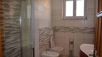 A bathroom with a glass shower enclosure, two toilets, and a sink.
