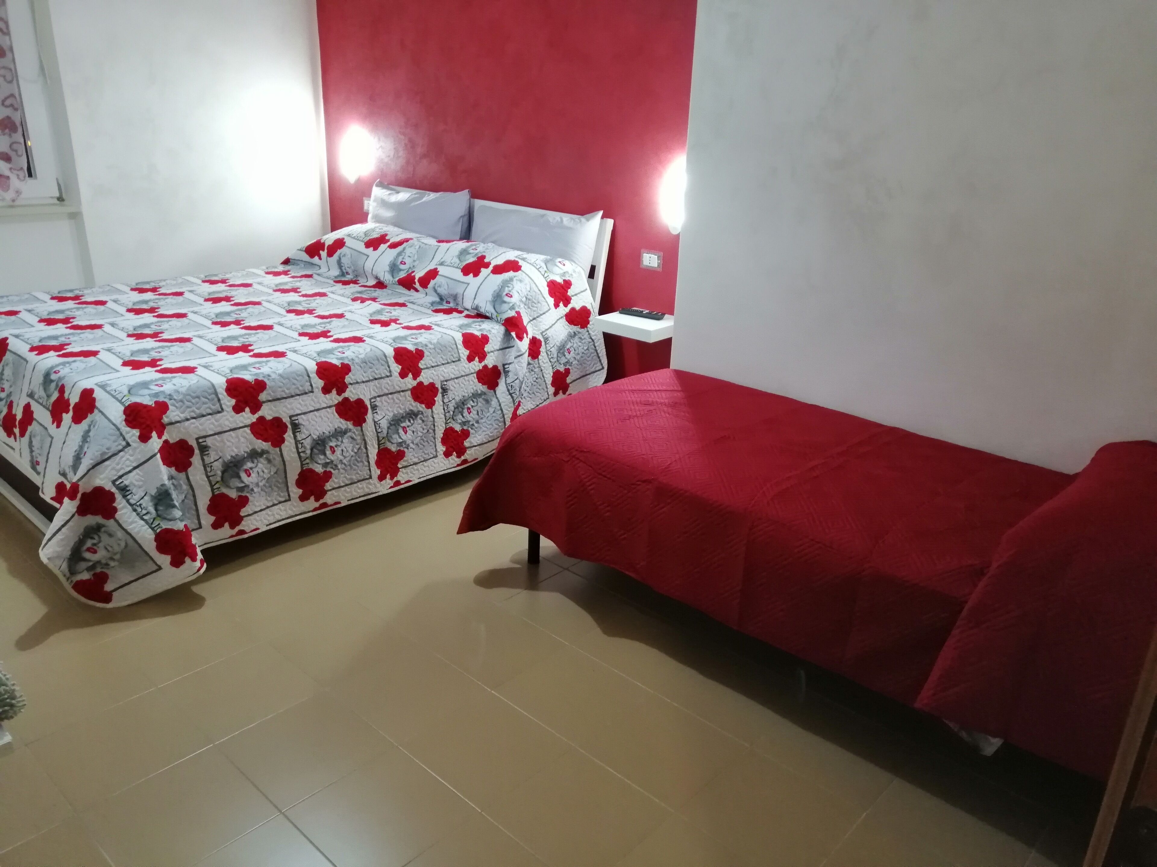 Quarto com duas camas, uma com colcha de padrão floral e a outra com colcha vermelha lisa.
