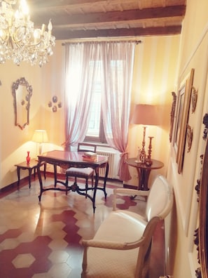 Quarto com mesa de madeira, uma cadeira, um lustre e janela com cortinas.