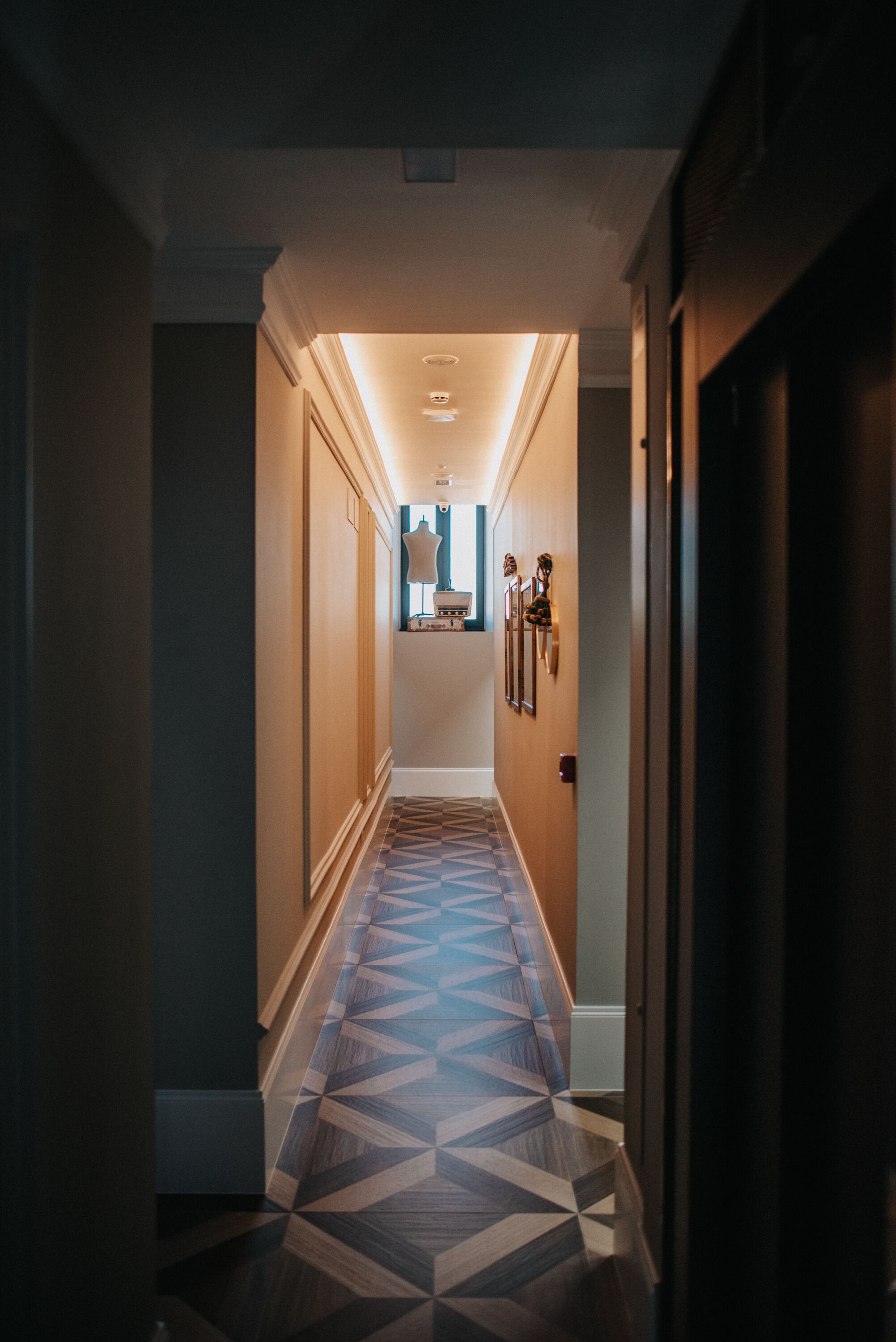 A hallway with patterned flooring, a light fixture on the ceiling, and framed pictures on the wall.