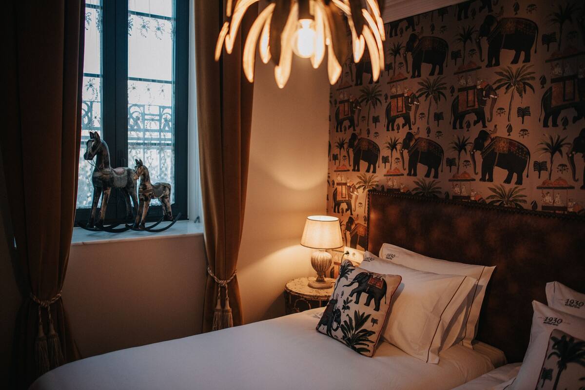 A bedroom with a bed, a nightstand, a lamp, and a window with curtains.