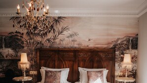 A double bed with a wooden headboard, two bedside tables with lamps, a chandelier, and a patterned rug. - 1930 Boutique Hotel (Arzua)