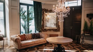 A room with a sofa, a round table, a chandelier, a mirror, and a patterned floor. - 1930 Boutique Hotel (Arzua)