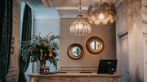 A reception desk with a vintage design, a potted plant, and a modern digital screen. - 1930 Boutique Hotel (Arzua)