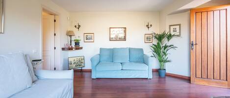 Una sala de estar con un sofá azul claro, un sofá blanco, piso de madera, alfombra estampada y una puerta de madera.