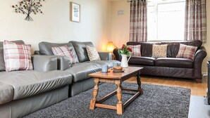 A modern living room with a grey sectional sofa, a wooden coffee table, and a grey carpet. - 4 bedroom accommodation in Nantglyn, near Denbigh (Nantglyn, near Denbigh)