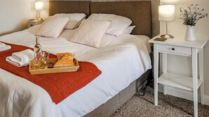 A neatly made bed with white linens, a red throw blanket, and a tray with a bottle, glasses, and a snack pack. - 4 bedroom accommodation in Nantglyn, near Denbigh (Nantglyn, near Denbigh)