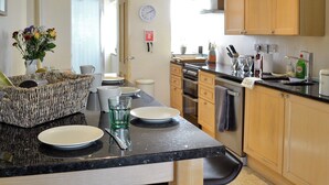 A modern kitchen with wooden cabinets, a granite countertop, and a dining area with a wicker basket and plates. - 4 bedroom accommodation in Nantglyn, near Denbigh (Nantglyn, near Denbigh)