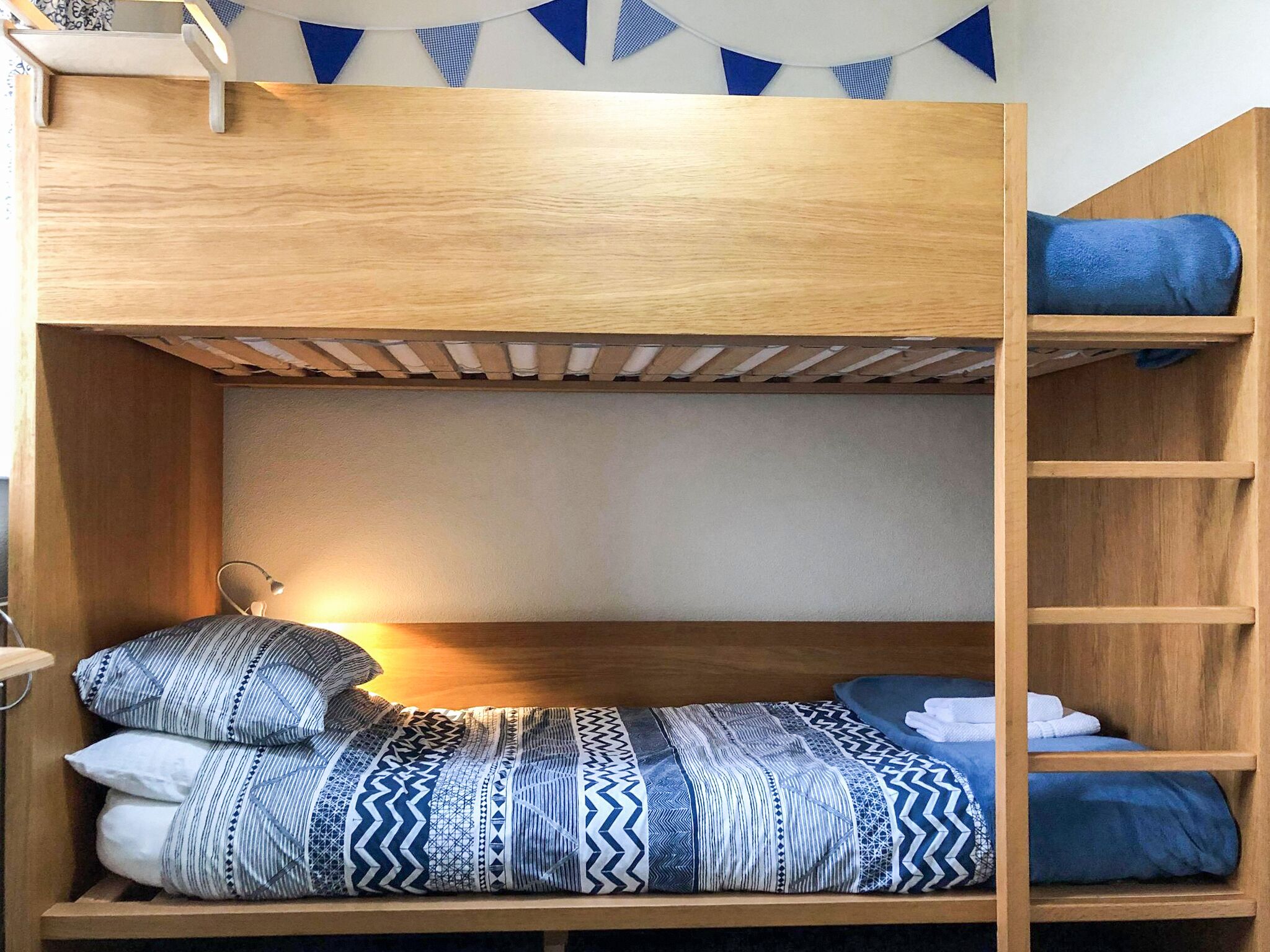 A bunk bed with a wooden frame, a patterned bedspread, and a blue blanket.