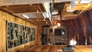 Een gezellig interieur van een blokhut met houten wanden, een groot kunstwerk aan de muur, een open haard en een houten eettafel.
