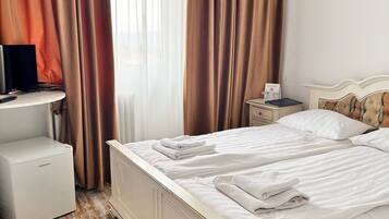 Habitación de hotel con cama, un escritorio pequeño con una computadora, una mesita de noche y televisor montado en la pared.