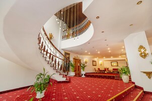 Una imponente escalera conduce a un comedor con alfombra roja y un techo alto con iluminación empotrada.