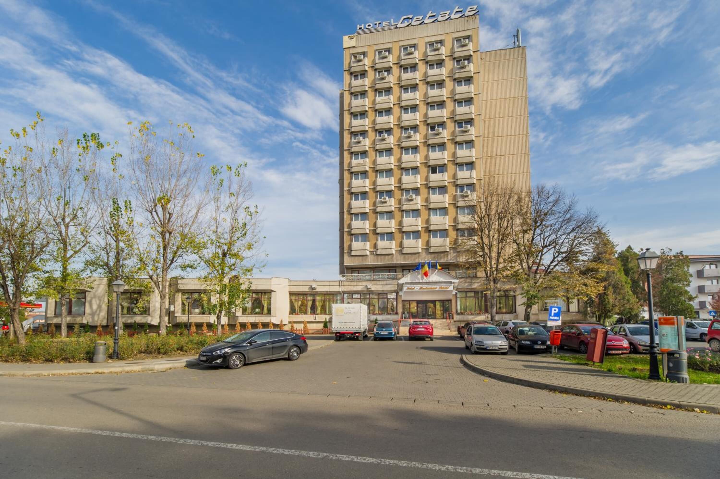Un bâtiment d’hôtel à la façade moderne, un espace de stationnement et un ciel dégagé.