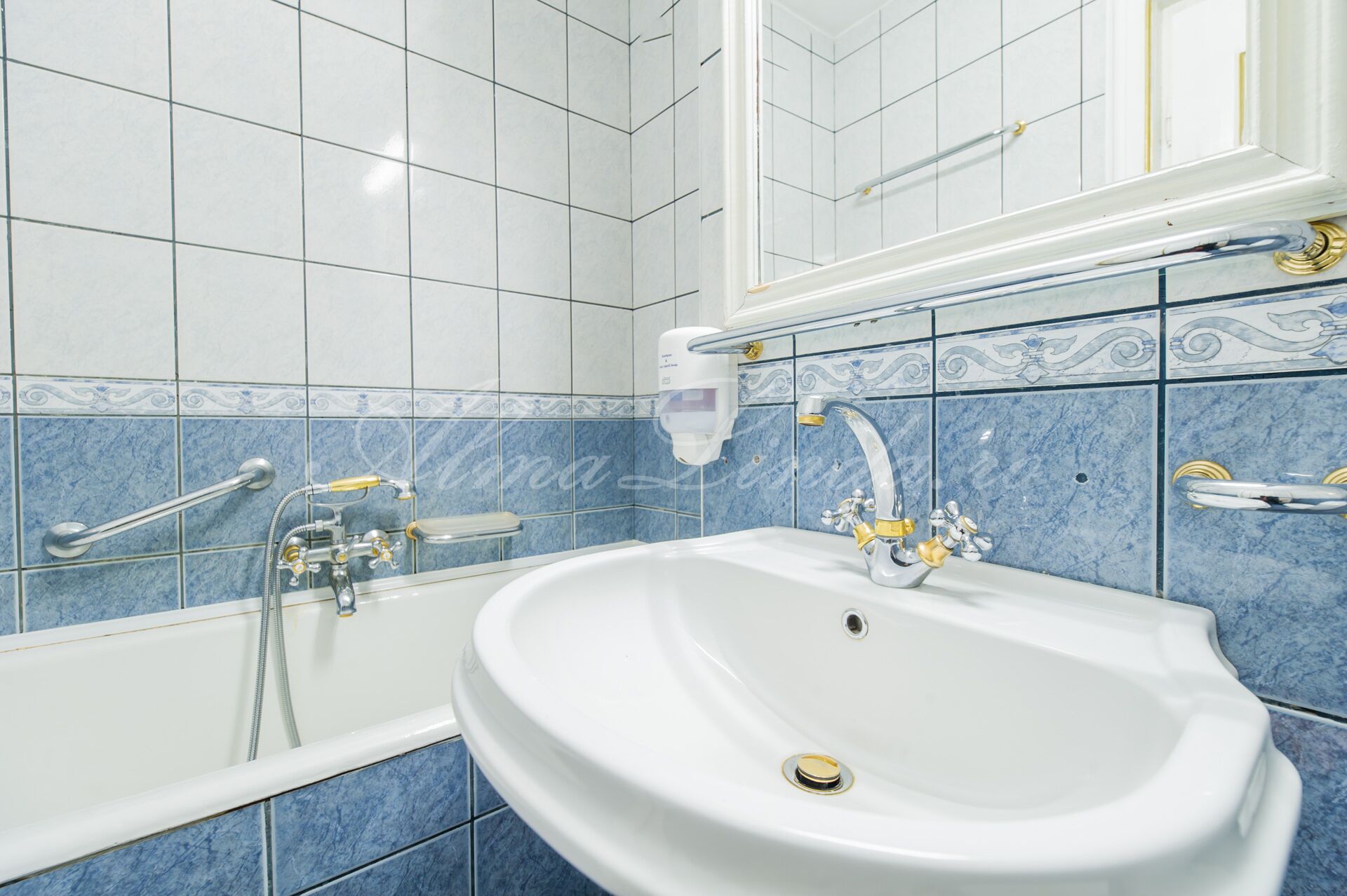 Un baño con un lavamanos blanco, una bañera con cabezal de ducha de mano y paredes con azulejos azules.