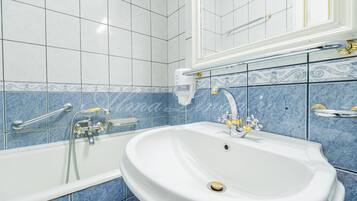 Un baño con un lavamanos blanco, una bañera con cabezal de ducha de mano y paredes con azulejos azules.