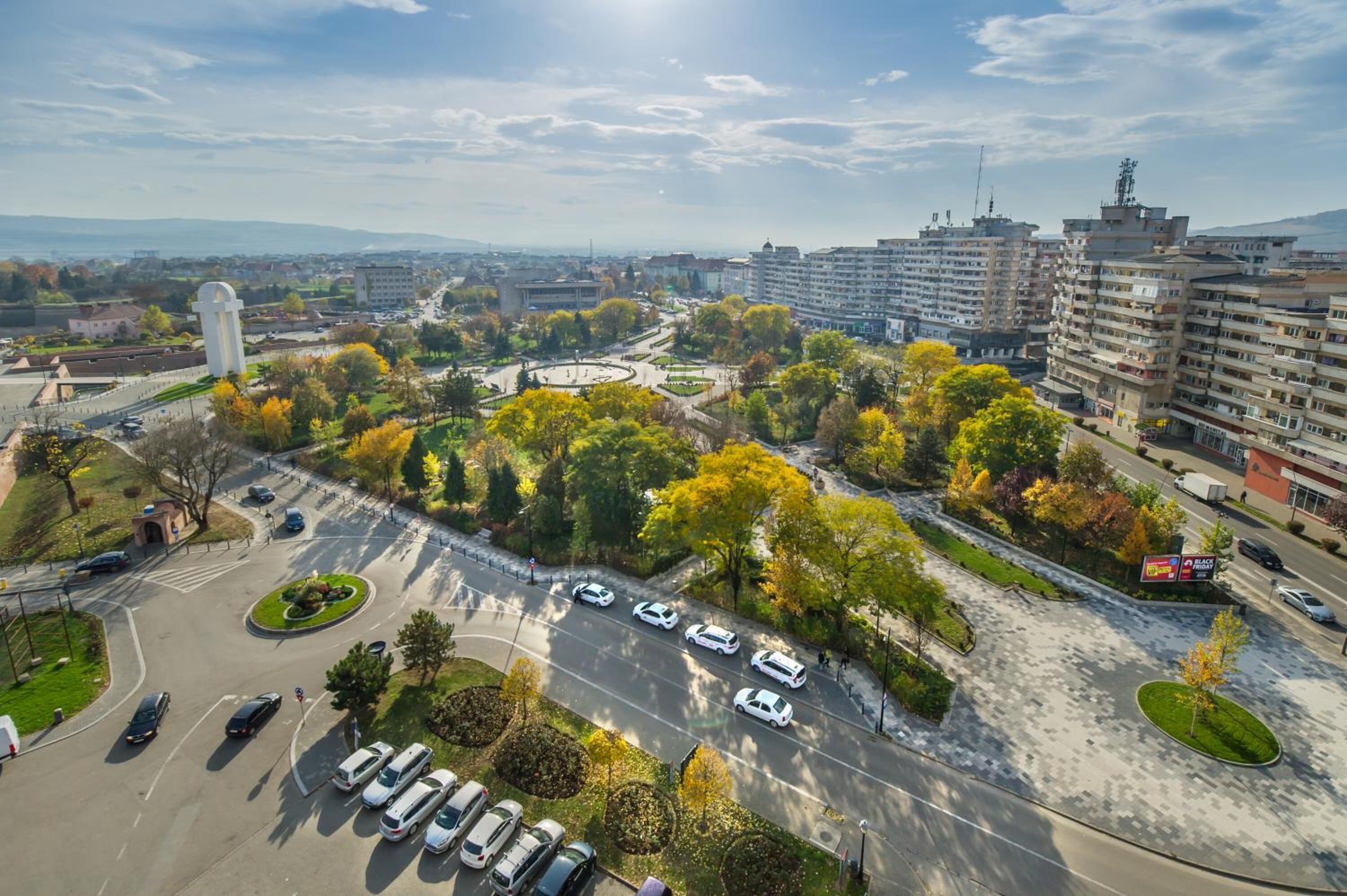An aerial view of a cityscape with a roundabout, buildings, and a parking lot.