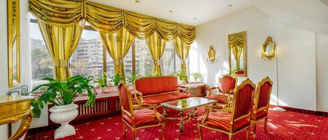 A room with a red carpet, gold curtains, and a sofa set.
