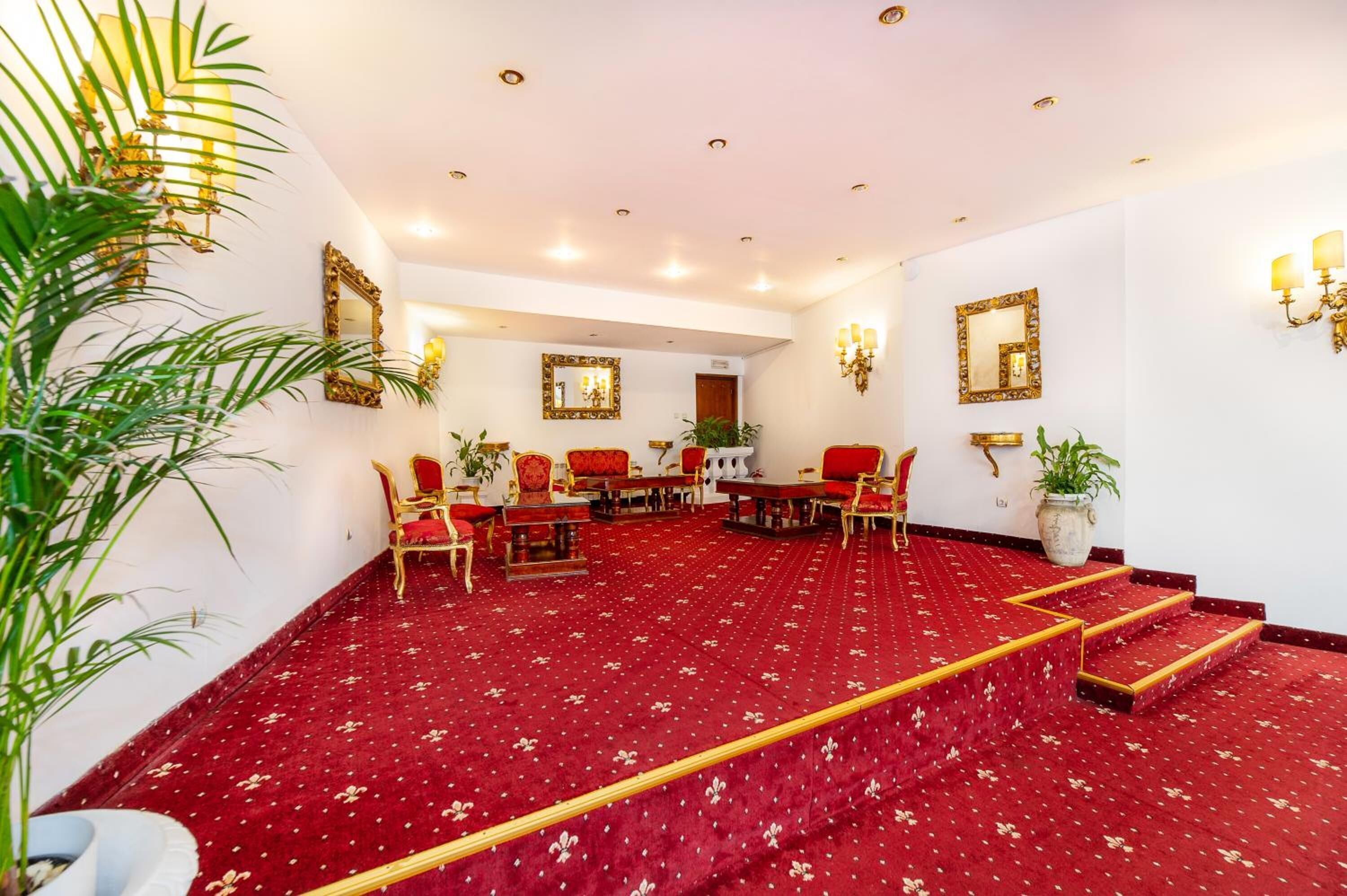 A hotel room with a red carpet, multiple seating areas, and decorative wall sconces.