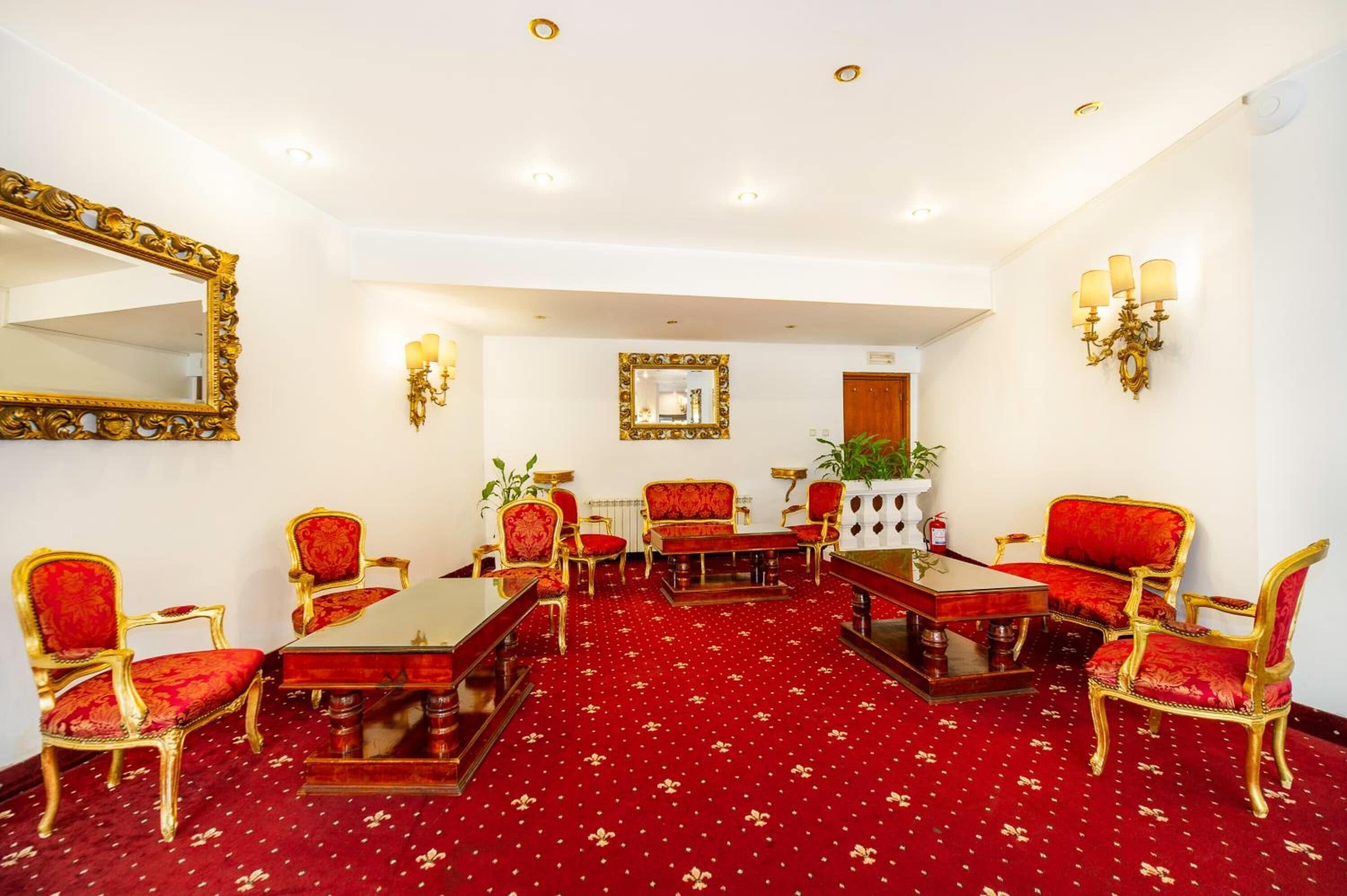 A formal meeting room with a red carpet, gold-framed chairs, a central table, and wall-mounted chandeliers.