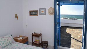 A bedroom with a bed, a nightstand, a wooden chair, and a view of the sea through an open door. - Naxos is the Way Summer Dream 3 apartment (Kastraki)