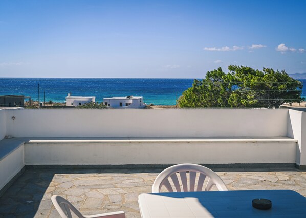 A terrace with a view of the sea, white buildings, and a tree.