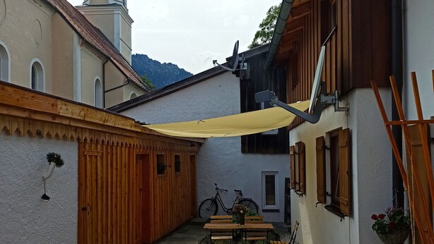 A courtyard with a wooden table and chairs, a bicycle, and a small garden with flowers. - Schönes Ammertal (Oberammergau)
