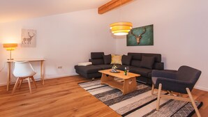 A modern living room with a wooden floor, a sofa, a coffee table, and two chairs. There is a lamp on a desk and artwork on the walls. - Schönes Ammertal (Oberammergau)