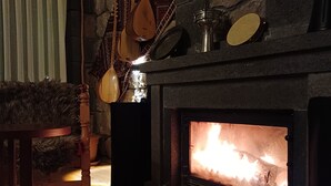Una chimenea de piedra con fuego, una mesa de madera y utensilios colgantes.