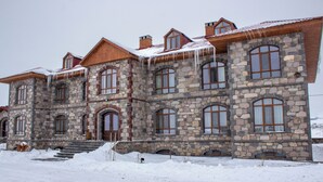 Un edificio de piedra grande con múltiples ventanas y techo de madera, rodeado de nieve.
