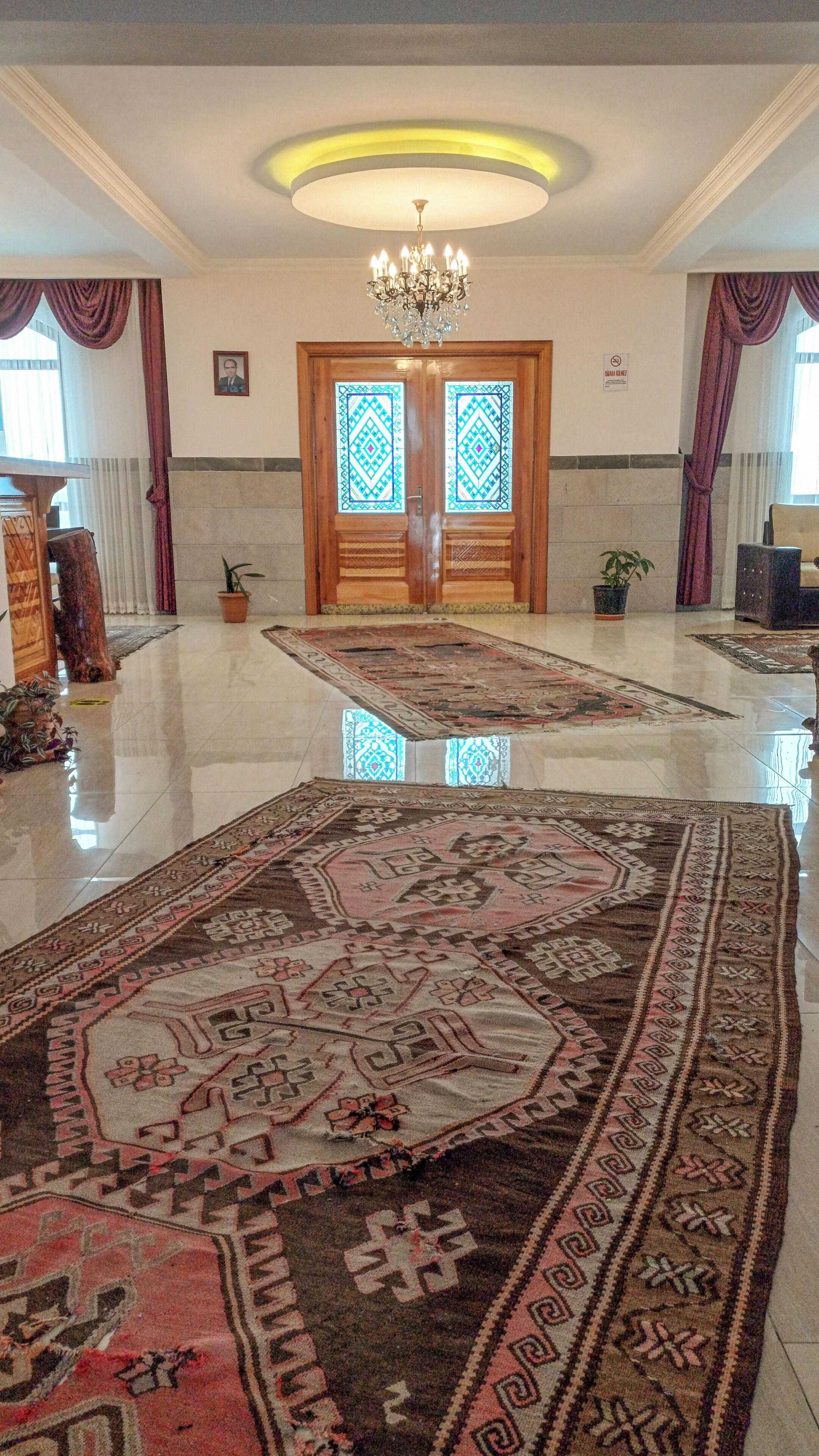 A spacious lobby with a chandelier, a large wooden door with intricate designs, and a polished floor.