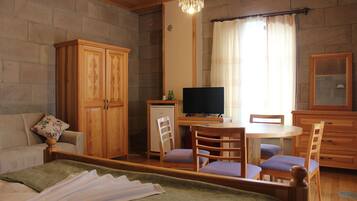 A bedroom with a bed, a desk with a computer, a television, and a dining area with chairs.