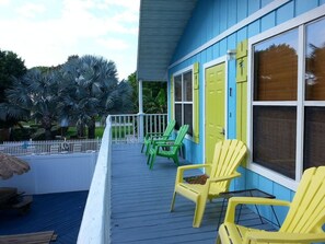 A porch with yellow Adirondack chairs, a white picket fence, and a blue building with yellow doors. - Steps from the beach 2BR @Manatee Beach (Holmes Beach)