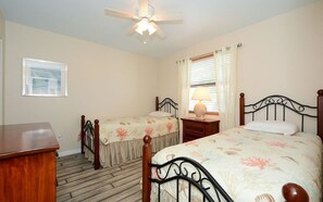 A bedroom with two single beds, a wooden dresser, a ceiling fan, and a window with blinds. - Steps from the beach 2BR @Manatee Beach (Holmes Beach)
