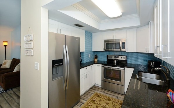 A modern kitchen with stainless steel appliances, white cabinets, and a blue tiled backsplash.