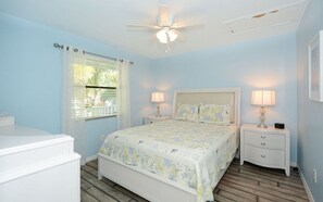A bedroom with a bed, two bedside tables, a ceiling fan, and a window with curtains.