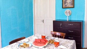 Un comedor con una mesa lista para dos personas, un mueble de color oscuro, una puerta blanca y un cuadro en la pared.