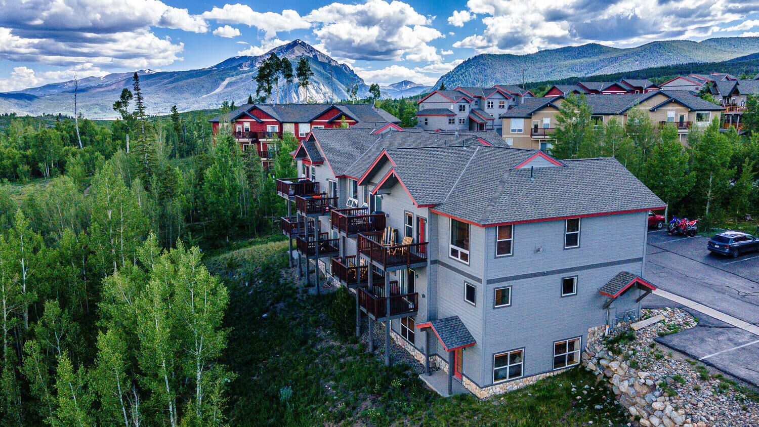 Un immeuble à plusieurs étages doté de balcons, entouré d’arbres et avec une montagne en arrière-plan.