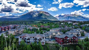 A residential area with multi-story houses, surrounded by dense forests and mountains in the background. - Exceptional Views, Large Townhome, Hot Tub, Pool, Private Garage 97A (Silverthorne)