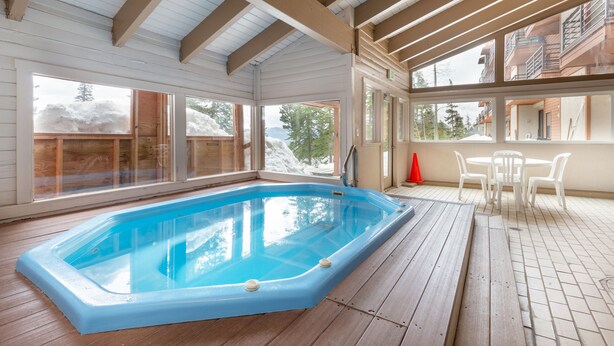 Una piscina interior con cubierta de madera, una mesa con sillas y vistas a un edificio con balcones.