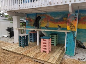 Une terrasse en bois agrémentée de tabourets colorés et d’une fresque représentant un coucher de soleil et la vie marine.