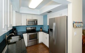 A compact kitchen with white cabinets, a stainless steel refrigerator, a microwave, and an oven. - Location! Steps from Manatee Beach 2BR (Holmes Beach)