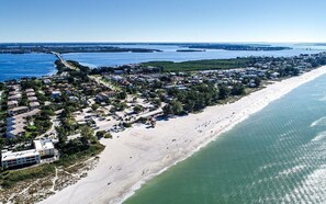 Vista aérea de un pueblo costero con una extensa playa de arena, una zona residencial densa y un puerto deportivo.
