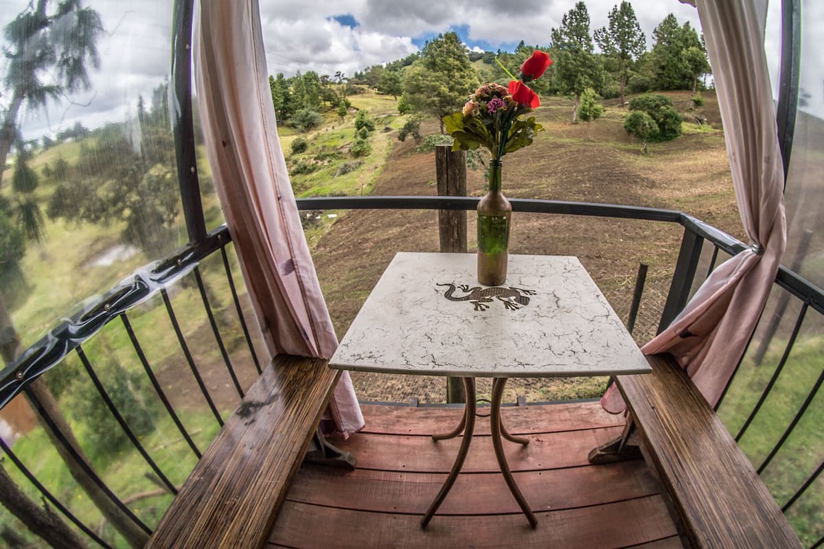 Un balcón con una mesa y un florero, con vistas a un paisaje rural.