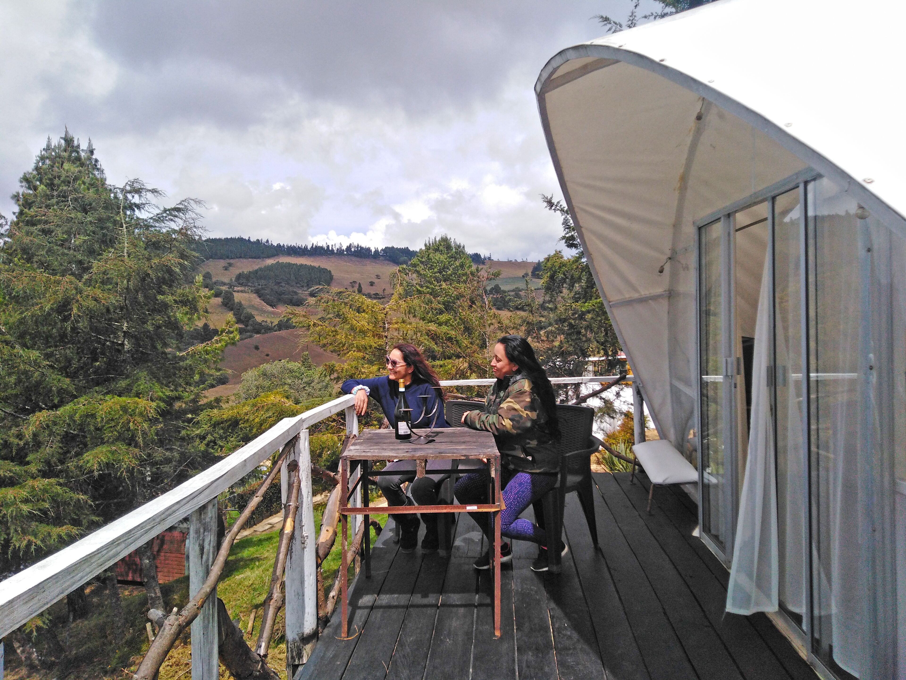 Una terraza de madera con una mesa y sillas, con vistas a un paisaje montañoso.