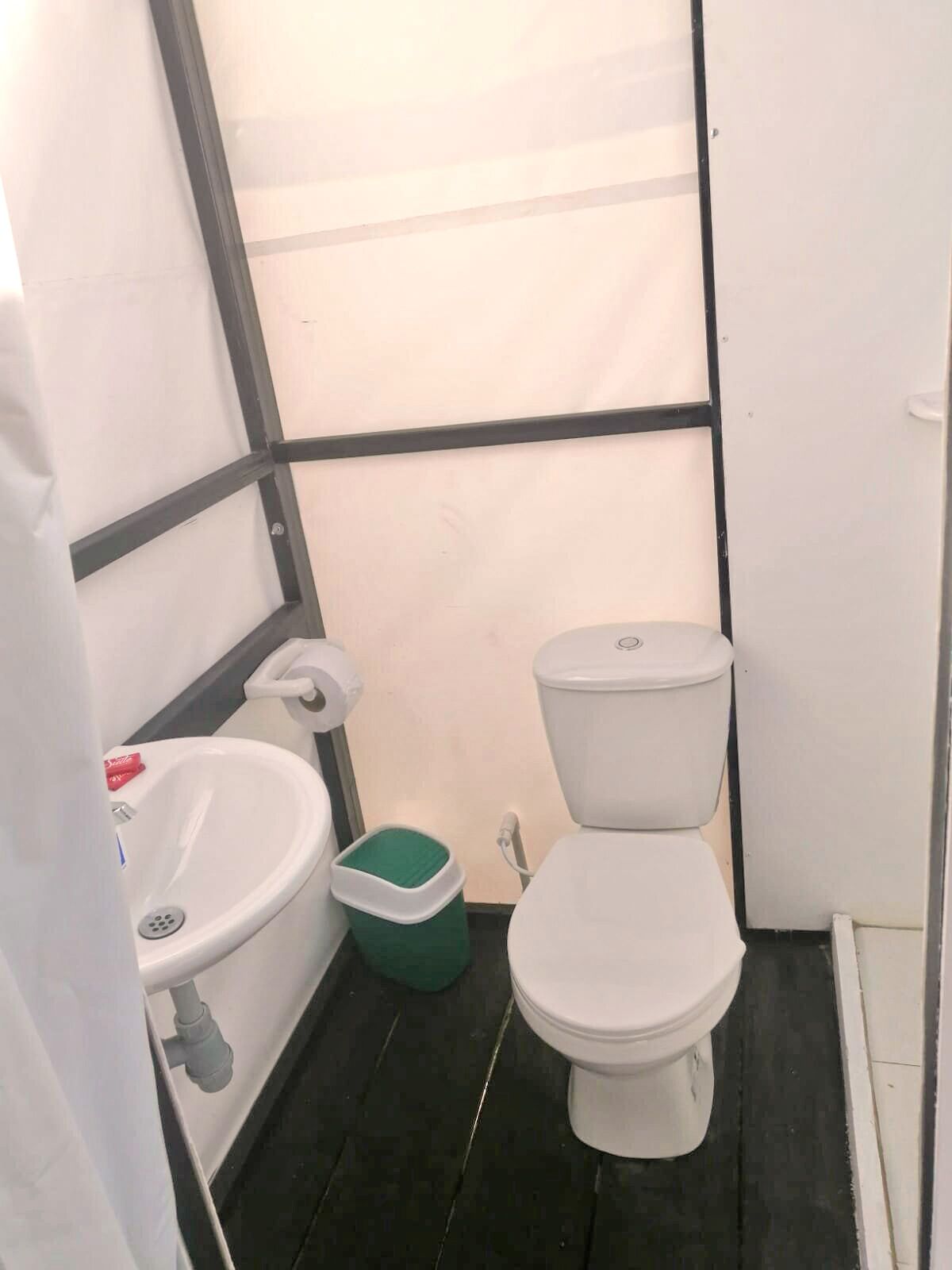Ein kleines, kompaktes Badezimmer mit einem weißen Waschbecken, einer Toilette und einer grünen Mülleimer.