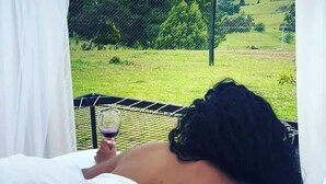 A person reclining in a bed with a view of a green landscape through a window with white curtains. - Tu Glamping (Chocontá)