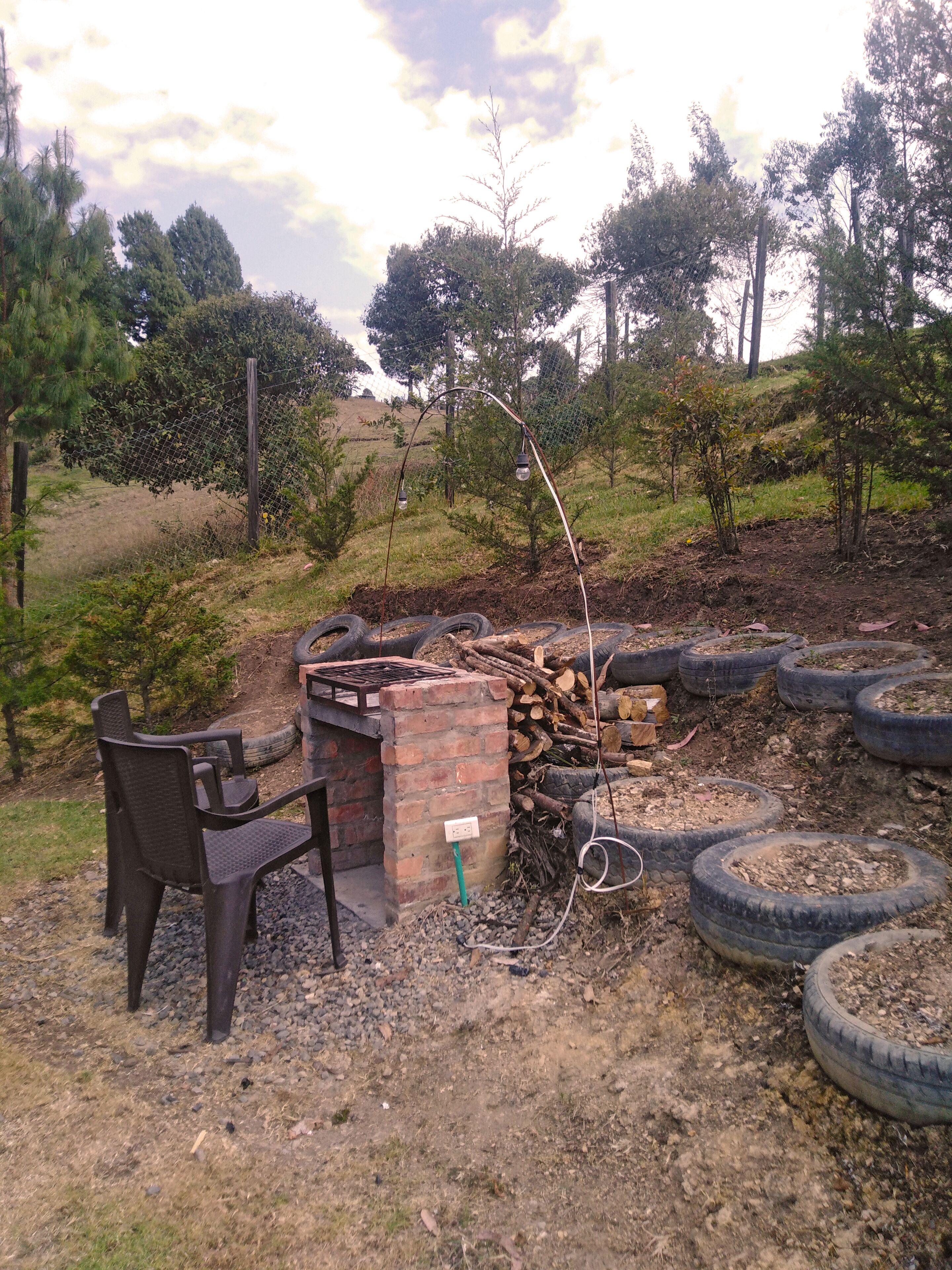 An outdoor seating area with a brick table and chairs, surrounded by tire planters and a wooden fence.
