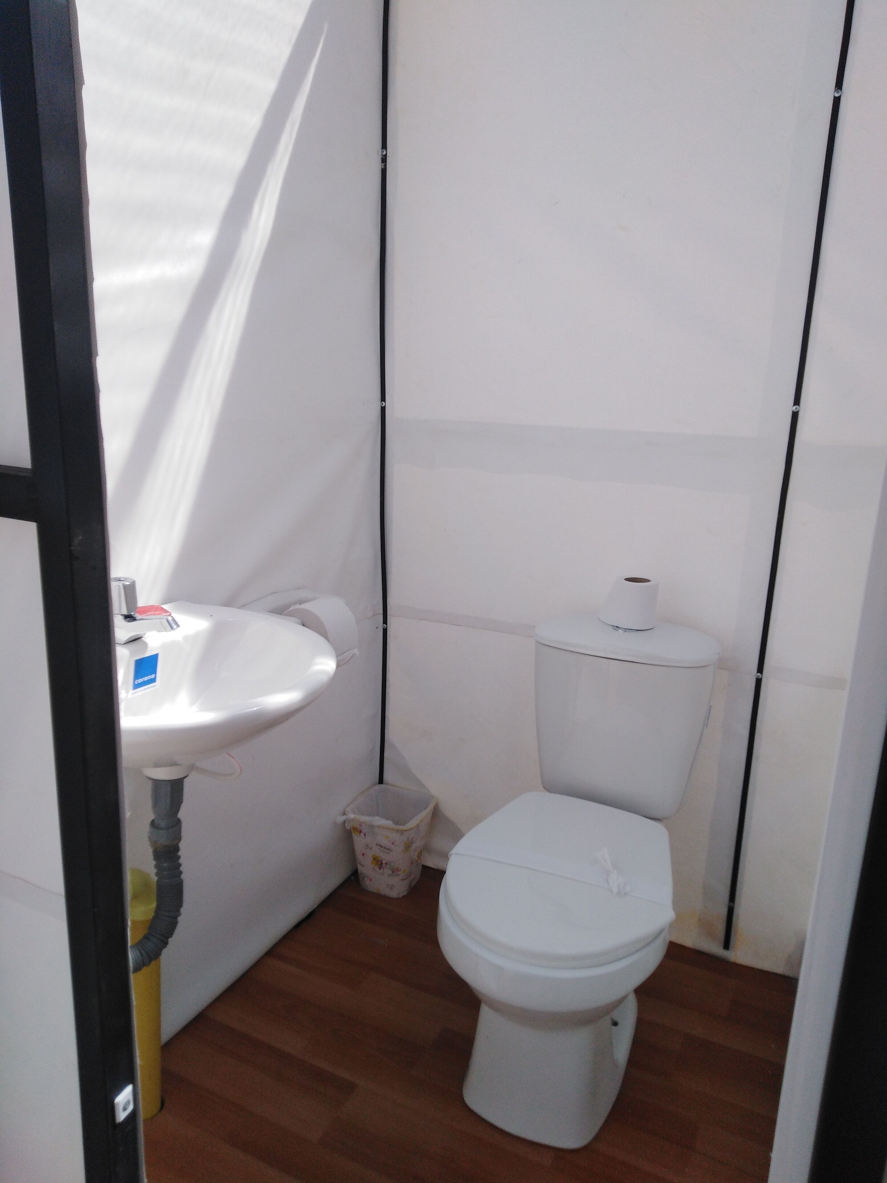 Un baño pequeño y funcional, con lavamanos, inodoro y cubo de basura blancos.